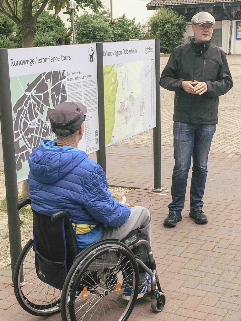 Ein Mitarbeiter von City Concepts und ein Rollstuhlfahrer stehen vor einer Startinfotafel.